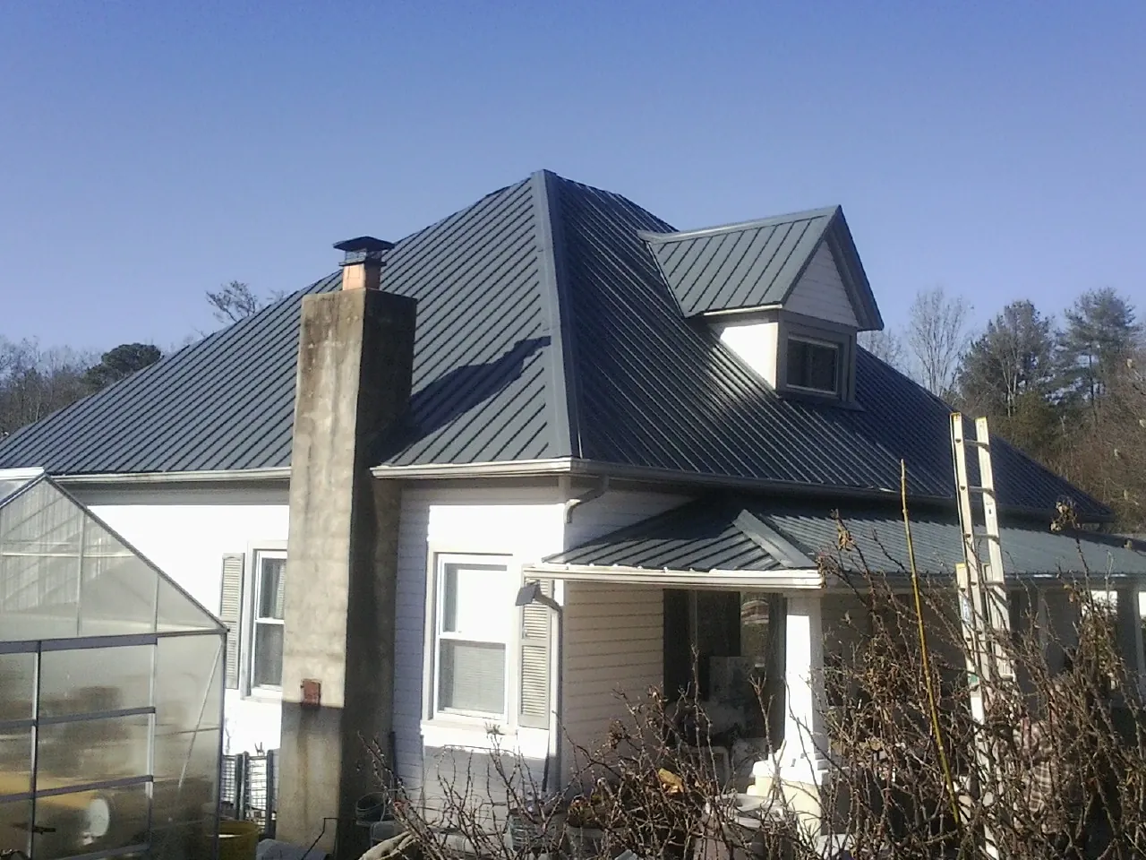 Dark blue standing seam metal roof on a white farmhouse with dormer — Slate & Tile Roof Repair by Roofing Brothers in Kenton