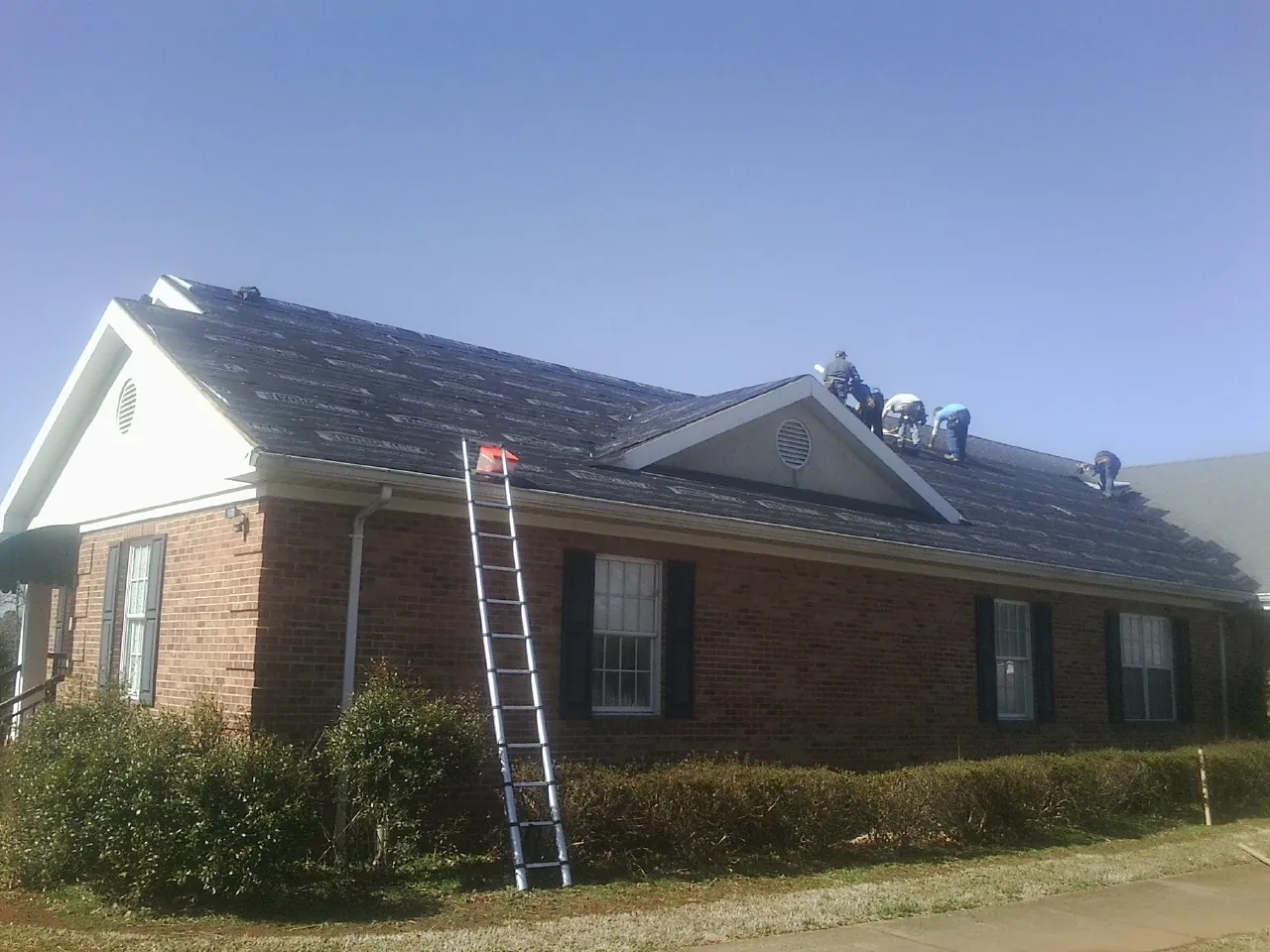 Crew tearing shingles off a brick ranch roof with a ladder set — Metal Roof Repair work by our crew in Kenton
