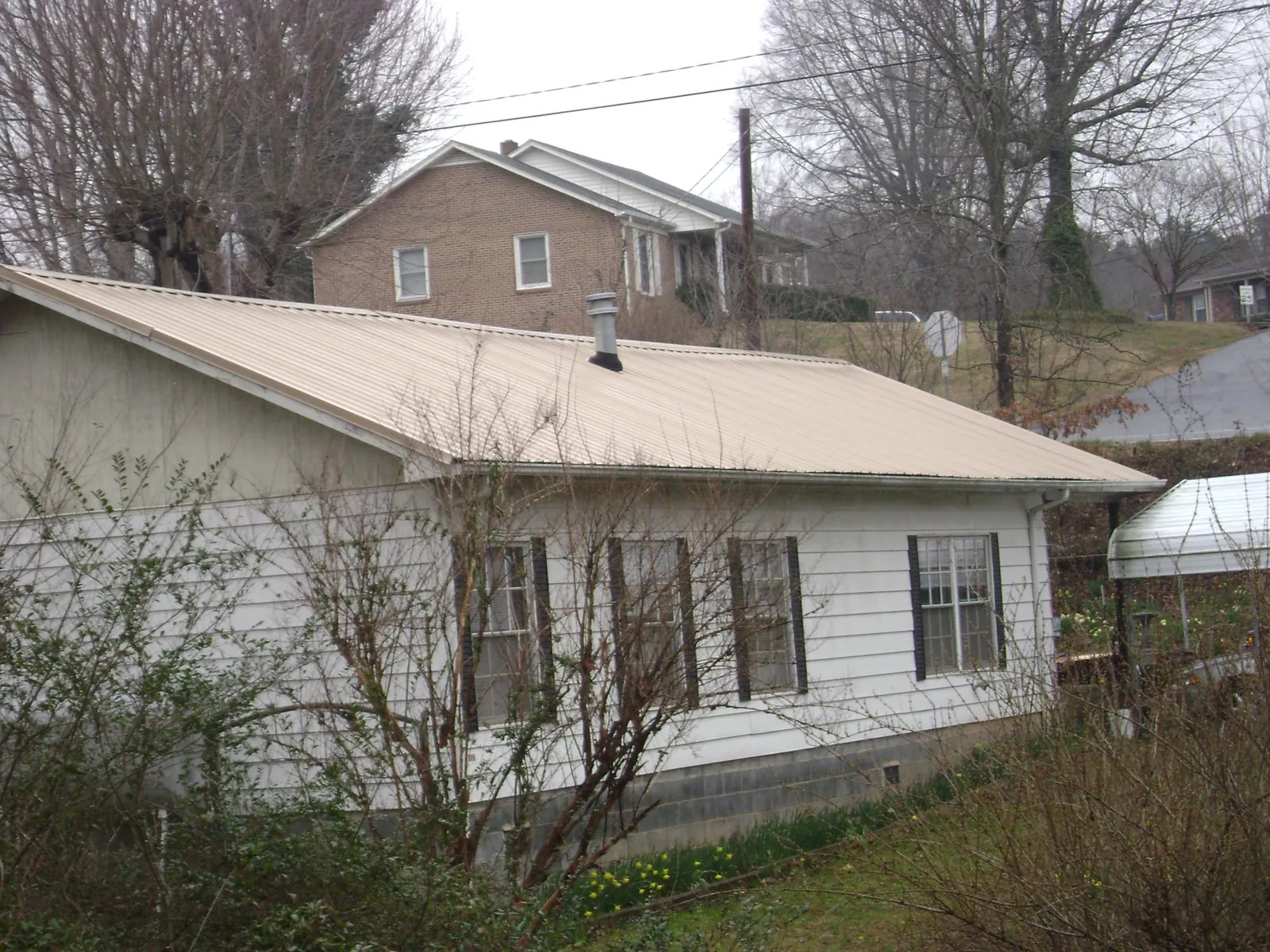 Tan metal roof on a white sided house set into a hillside — Commercial Roofing by Roofing Brothers in Kenton